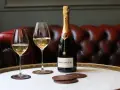 Bouteille de champagne Bollinger et deux verres remplis de champagne sur un plateau, avec un canapé en cuir rouge en arrière-plan.