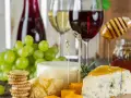 Un plateau de fromages, raisins verts, biscuits et miel dégoulinant sur un morceau de bleu, avec un verre de vin rouge léger en arrière-plan.