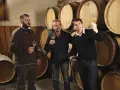 Trois hommes dégustent du vin dans la cave du domaine des Gandines, entourés de fûts de chêne.