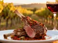 Un plat d'agneau rôti avec une sauce savoureuse, accompagné d'un verre de vin rouge, dans un décor de vignoble. Idéal pour savoir quel vin avec agneau.