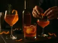 Trois cocktails ambrés, dont un avec une écorce d'orange et du romarin. Un barman prépare un autre verre avec du vin d'orange avec peau.