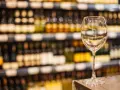 Verre à vin vide sur un comptoir, devant des étagères remplies de bouteilles. L'ambiance évoque une foire aux vins de printemps.