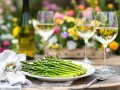 Un plateau d'asperges vertes fraîches, une bouteille de vin blanc et deux verres remplis de vin, parfaits pour savoir quel vin avec asperges.