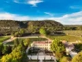 Vue aérienne du **château Beaulieu**, un domaine viticole pittoresque entouré de vignobles et d'une colline boisée. On imagine Nicolas **Sarkozy** y savourer un bon vin.