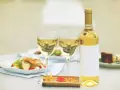 Une bouteille de vin blanc et deux verres sur une table, avec des salades et un dessert. Un clin d'œil à Alexandre de Lur Saluces.