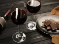 Deux verres de vin rouge, une bouteille et une assiette de chocolat, prêts pour un accord vin chocolat parfait.