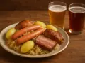 Assiette de choucroute garnie avec saucisses, lard, pommes de terre et deux verres de bière. Un repas copieux, parfait avec une bière ou un vin blanc.
