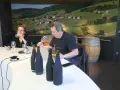 Dégustation de vins au domaine Mugneret Gibourg. Un homme et une femme goûtent du vin devant des bouteilles et un paysage de vignobles.