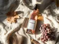 Bouteille de vin vegan rosé, posée sur un tissu beige, avec des grappes de raisin et des feuilles d'automne.