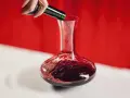 Une main verse un vin rouge profond dans une carafe. Ce pourrait être le meilleur vin du Cabardès, prêt à être savouré.