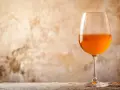 Verre de vin de macération à la couleur ambrée, sur un fond texturé et une table en bois.