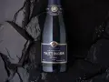 Bouteille de champagne Taittinger Prélude Grands Crus sur fond sombre, avec des paillettes scintillantes. Un avis sur ce champagne est à découvrir.