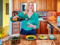 Une femme verse du vin vert dans un verre, avec une salade et des pains plats sur le comptoir.