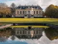 Le château La Louvière, majestueux, se reflète dans un étang paisible, entouré d'arbres aux couleurs d'automne.