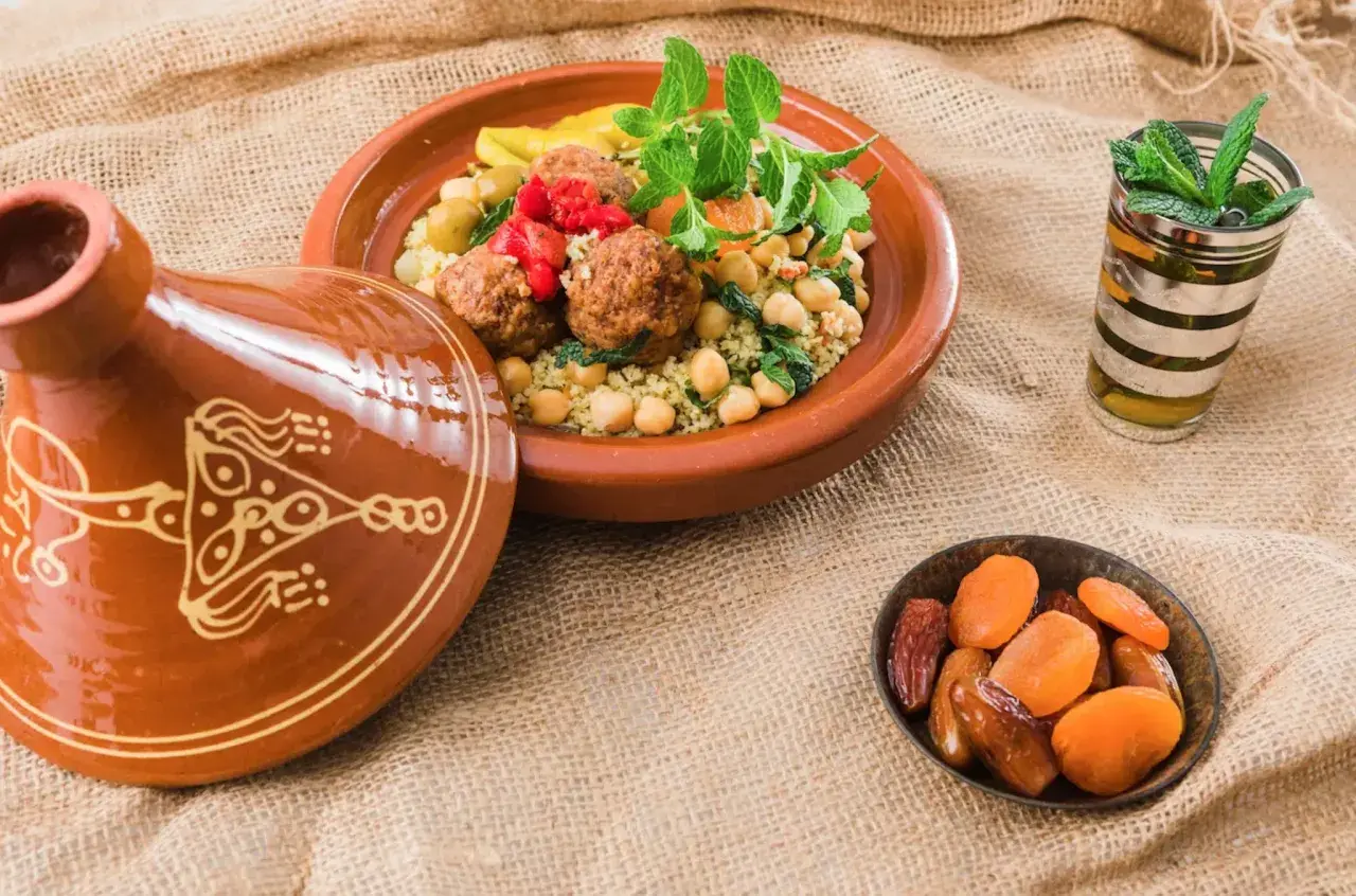 Un plat de couscous aux boulettes de viande, garni de menthe fraîche, accompagné d'un verre de thé à la menthe et de fruits secs. Un délice pour accompagner un bon vin.