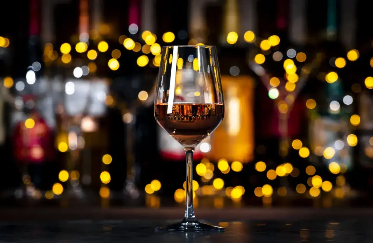 Un verre de vin orange scintille, reflétant les lumières chaudes d'un bar animé.