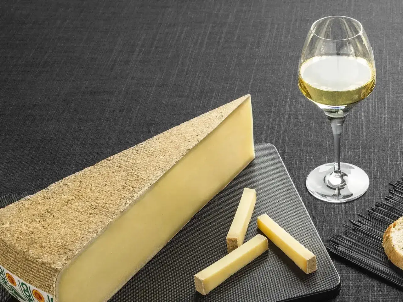 Un morceau de fromage à pâte dure et quelques bâtonnets, accompagnés d'un verre de vin blanc sucré et d'une tranche de pain.
