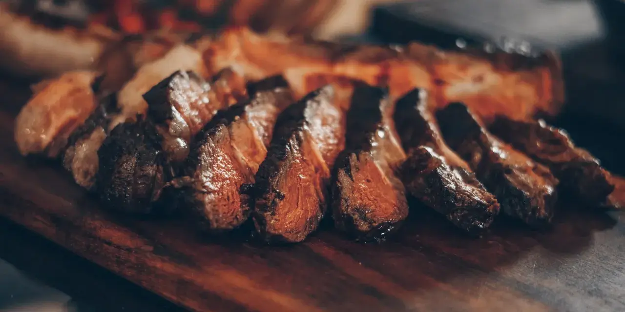 Tranches de viande grillée sur une planche en bois. Idéal pour savoir que boire avec une pierrade viande.
