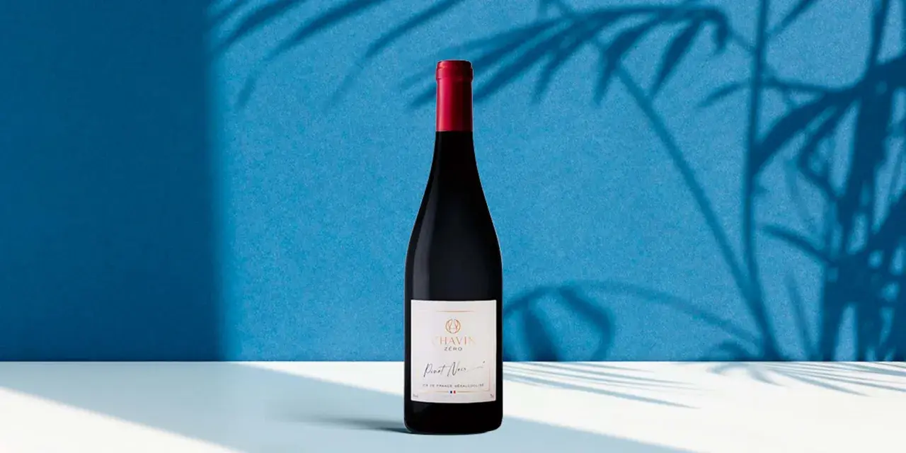 Bouteille de Pinot Noir Chavin Zero, le meilleur vin sans alcool, sur fond bleu avec des ombres de feuilles.