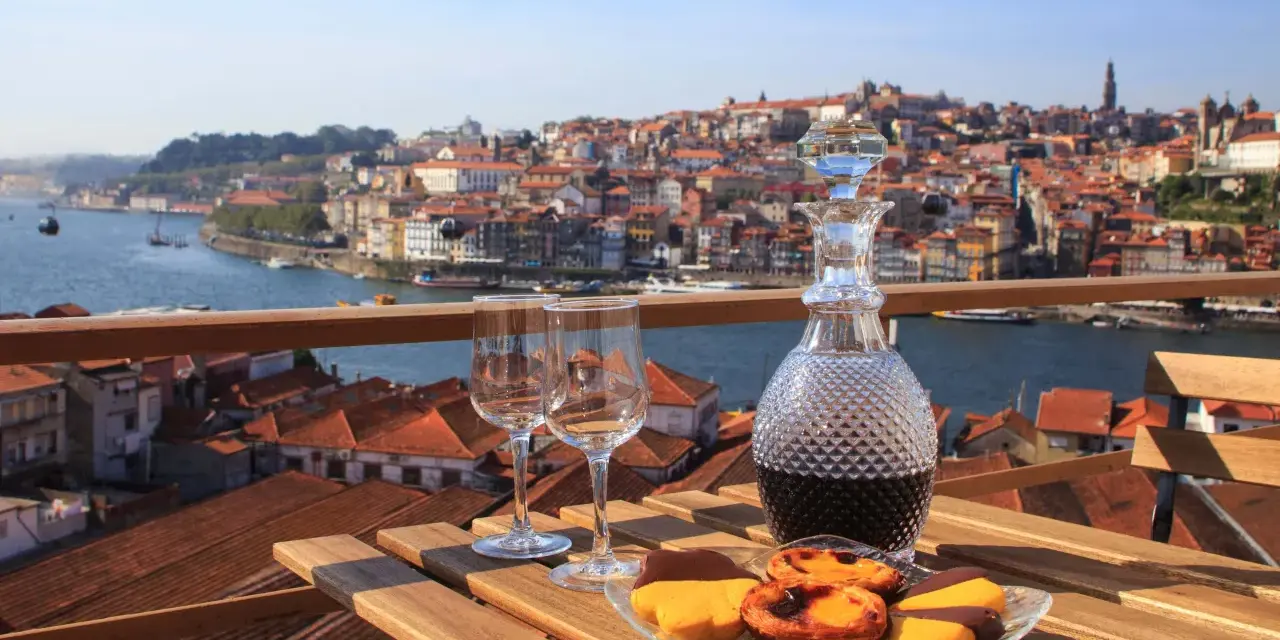 Verre de porto tawny ou ruby, deux verres à vin et des pâtisseries sur une table en bois, avec la ville de Porto en arrière-plan.