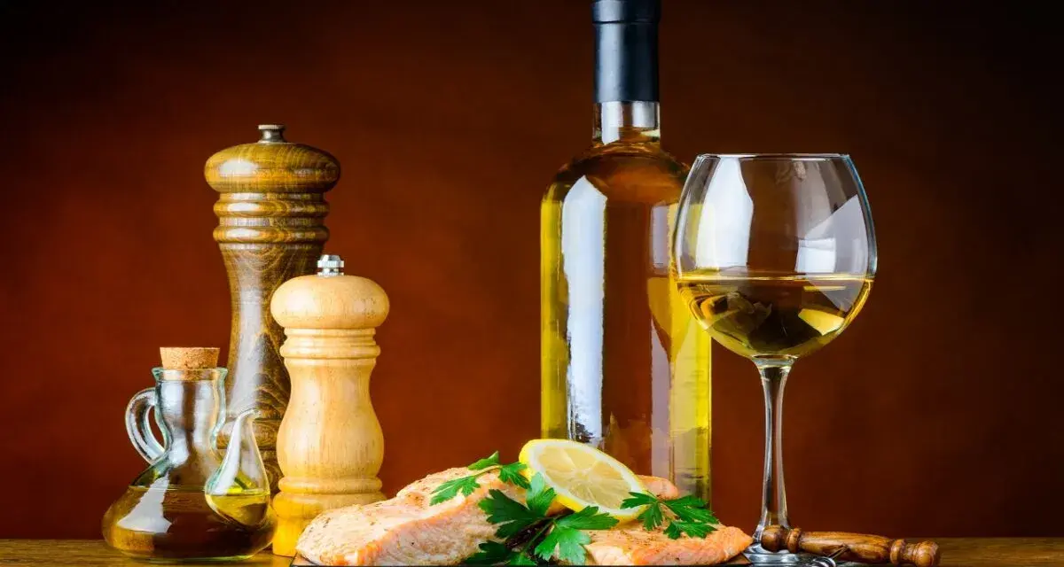 Un plat de saumon avec citron et persil, accompagné d'une bouteille et d'un verre de vin blanc, moulin à poivre et salière, huile d'olive. Le meilleur vin blanc pour cuisiner est prêt.