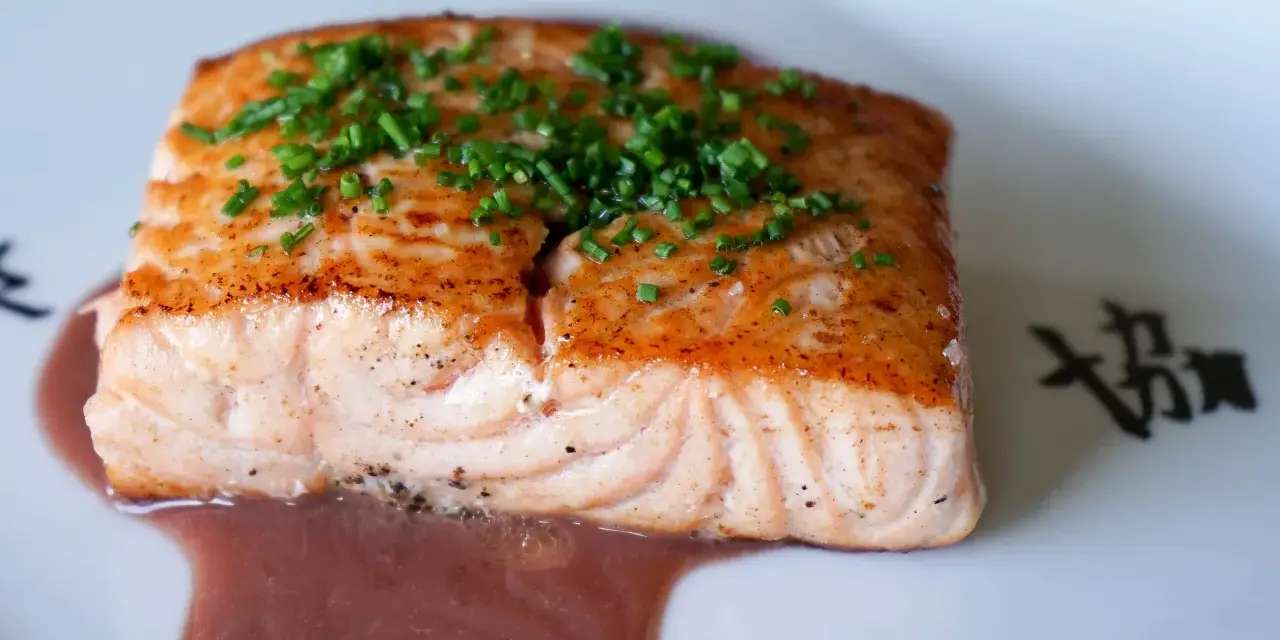 Un filet de saumon cuit, garni de ciboulette, baignant dans une sauce rouge. Un délice qui invite à se demander quel vin rouge avec du saumon cuit serait parfait.