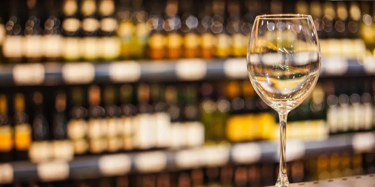 Verre à vin vide sur un comptoir, devant des étagères remplies de bouteilles. L'ambiance évoque une foire aux vins de printemps.