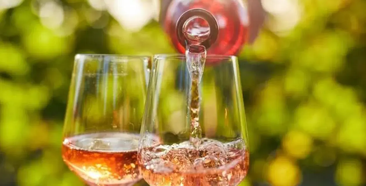 Un verre de rosé est servi dans un autre verre, sous un soleil radieux. Un moment parfait pour boire du rosé tous les jours.