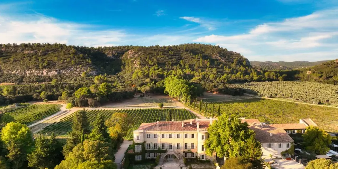 Vue aérienne du **château Beaulieu**, un domaine viticole pittoresque entouré de vignobles et d'une colline boisée. On imagine Nicolas **Sarkozy** y savourer un bon vin.