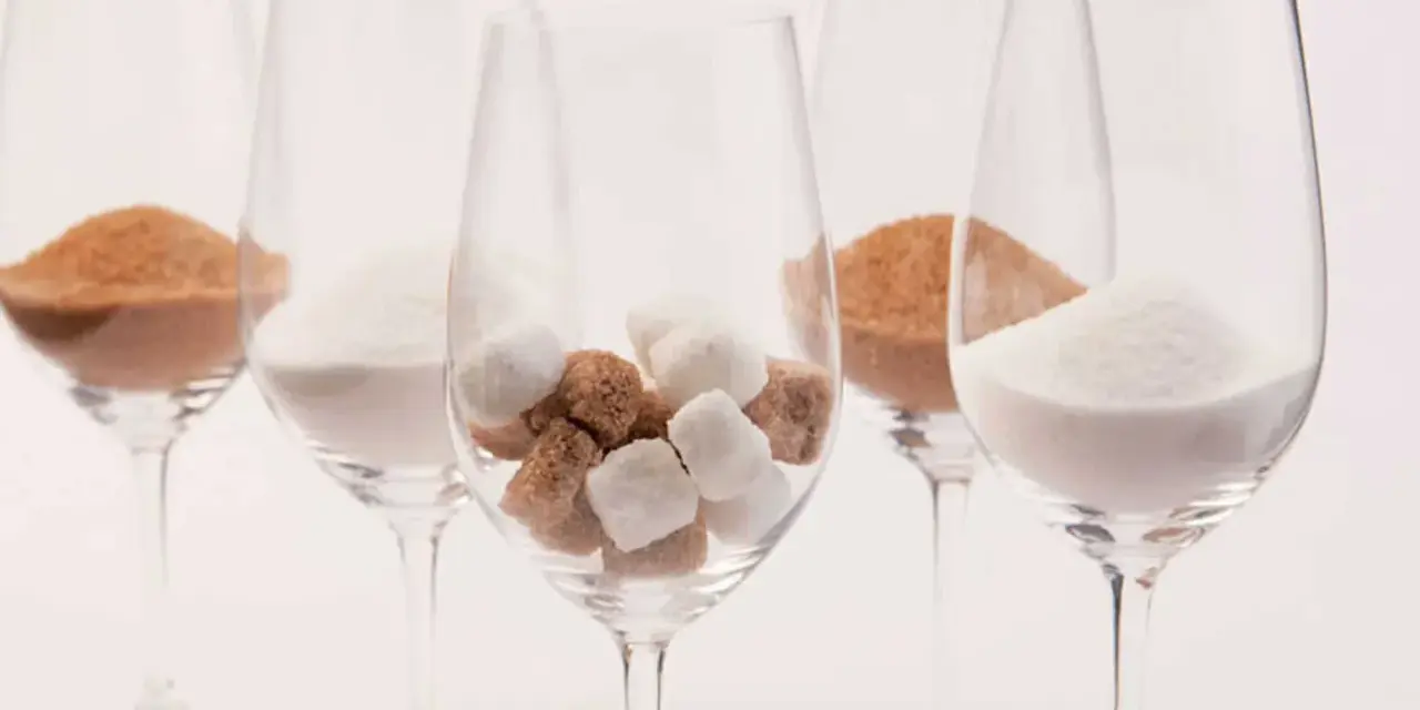 Cinq verres à vin contiennent différentes formes de sucre : du sucre en poudre blanc, du sucre brun en poudre et des morceaux de sucre blanc et brun. Une métaphore visuelle du sucre dans le vin.
