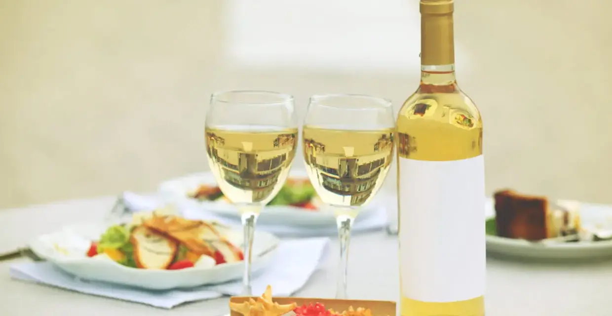 Une bouteille de vin blanc et deux verres sur une table, avec des salades et un dessert. Un clin d'œil à Alexandre de Lur Saluces.