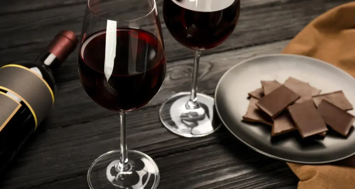 Deux verres de vin rouge, une bouteille et une assiette de chocolat, prêts pour un accord vin chocolat parfait.