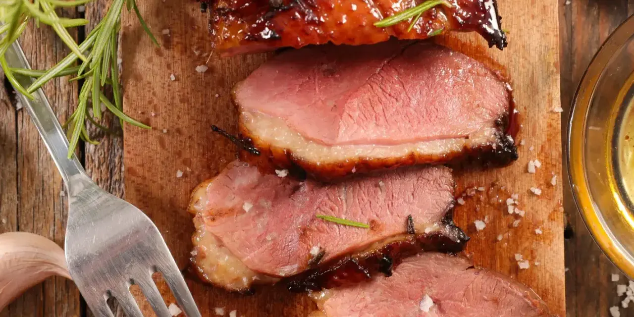 Tranches de magret de canard juteux, garnies de romarin et de sel, prêtes à être dégustées avec un verre de vin.