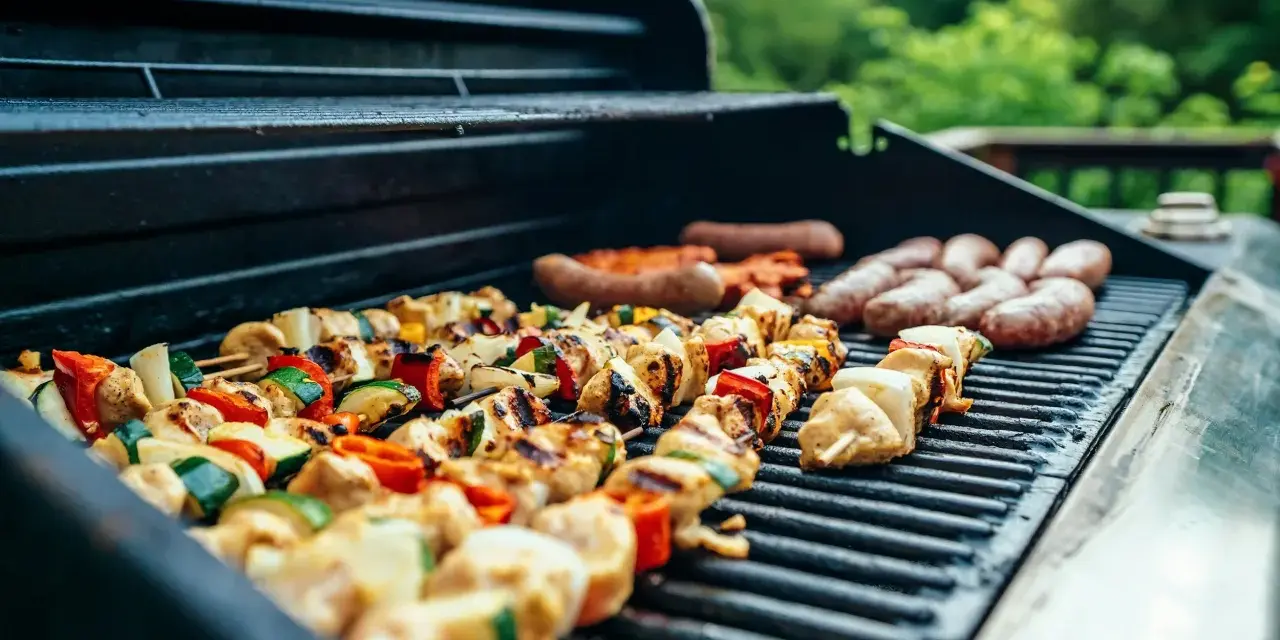 Brochettes de poulet et légumes grillés sur un barbecue, accompagnées de saucisses. Parfait pour un barbecue d'été avec un verre de vin blanc.