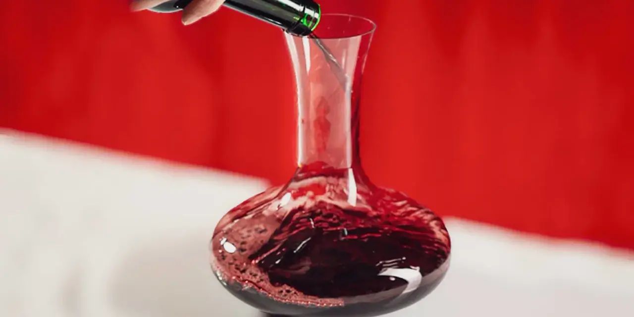 Une main verse un vin rouge profond dans une carafe. Ce pourrait être le meilleur vin du Cabardès, prêt à être savouré.
