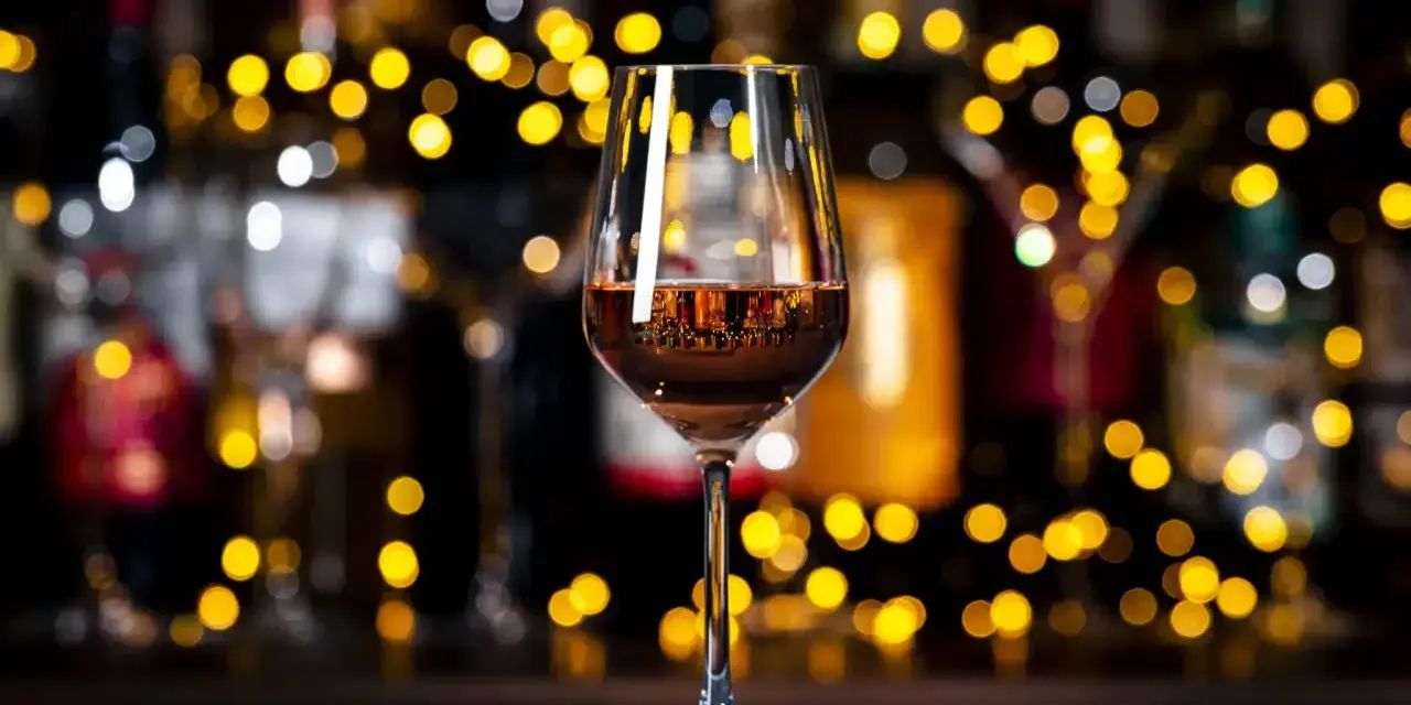 Un verre de vin orange scintille, reflétant les lumières chaudes d'un bar animé.