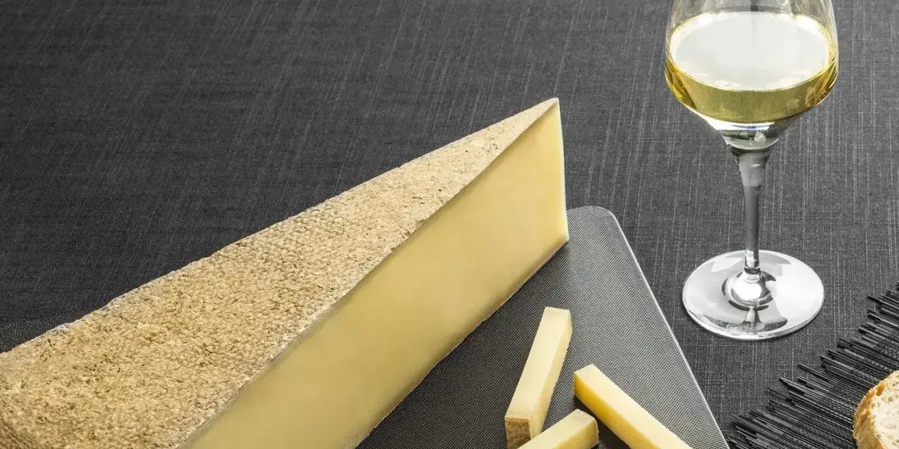 Un morceau de fromage à pâte dure et quelques bâtonnets, accompagnés d'un verre de vin blanc sucré et d'une tranche de pain.