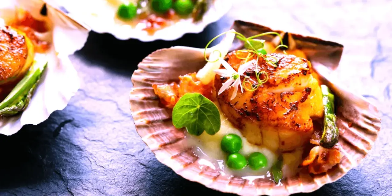 Saint-jacques poêlées, tendres et dorées, servies dans leur coquille avec des petits pois et une touche de vin rouge.