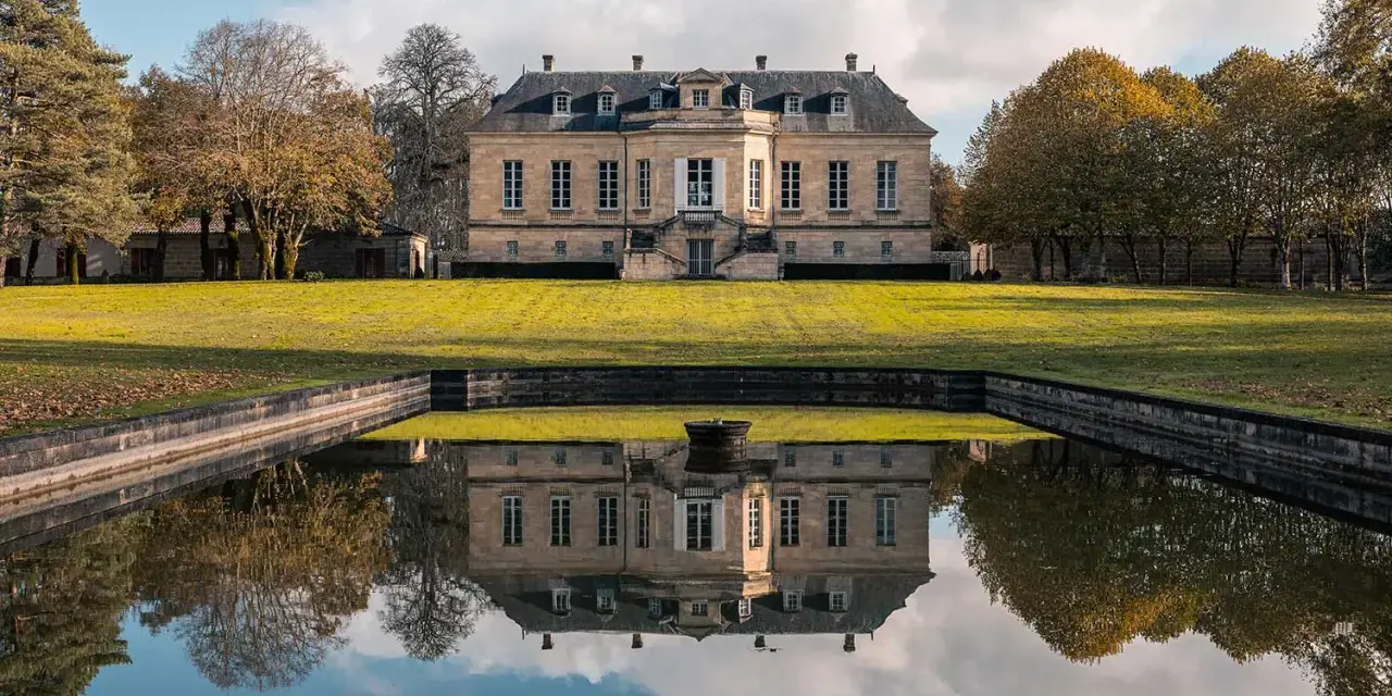 Le château La Louvière, majestueux, se reflète dans un étang paisible, entouré d'arbres aux couleurs d'automne.