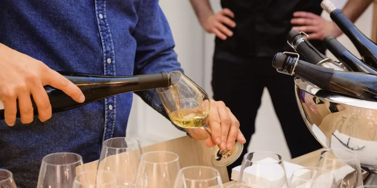 Un homme verse du vin blanc, peut-être un pinot gris, dans un verre. Il sera parfait avec du poisson.