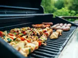 Brochettes de poulet et légumes grillés sur un barbecue, accompagnées de saucisses. Parfait pour un barbecue d'été avec un verre de vin blanc.