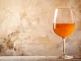 Verre de vin de macération à la couleur ambrée, sur un fond texturé et une table en bois.
