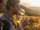 Un homme et une femme dégustent un vin jaune du Jura au coucher du soleil, dans un vignoble aux couleurs d'automne.