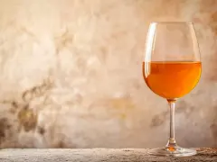 Verre de vin de macération à la couleur ambrée, sur un fond texturé et une table en bois.