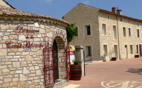 Bienvenue au **domaine de la Croix Blanche**. Une bâtisse en pierre avec une enseigne élégante et une porte ornée de ferronneries rouges.