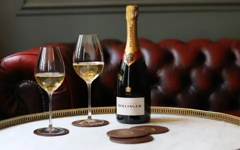 Bouteille de champagne Bollinger et deux verres remplis de champagne sur un plateau, avec un canapé en cuir rouge en arrière-plan.