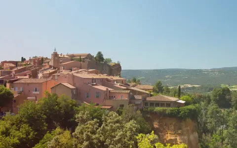 Village perché aux toits de tuiles roses, entouré de verdure. Au loin, des collines rappellent les vignes oubliées d'une Provence intemporelle.