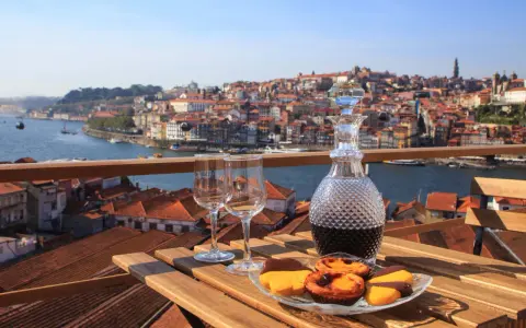 Verre de porto tawny ou ruby, deux verres à vin et des pâtisseries sur une table en bois, avec la ville de Porto en arrière-plan.