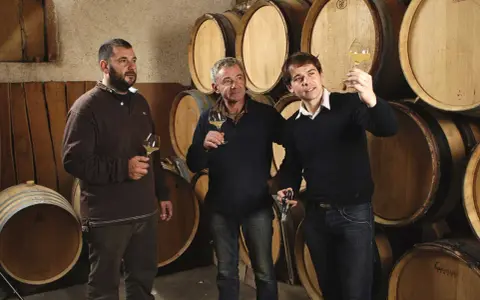 Trois hommes dégustent du vin dans la cave du domaine des Gandines, entourés de fûts de chêne.