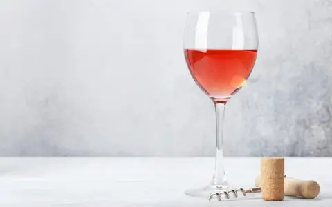 Un verre de bon rosé, prêt à être dégusté, avec un tire-bouchon et un bouchon à proximité.